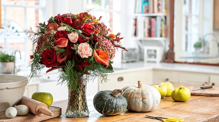 یک گلدان پر از گل روی میز با دکور پاییزی